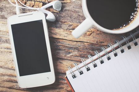 Blank notepad and smart phone with hot coffee on office tableの写真素材