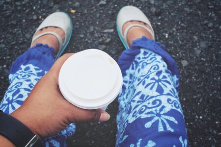 Selfie of coffee paper cup on hand with feetの写真素材