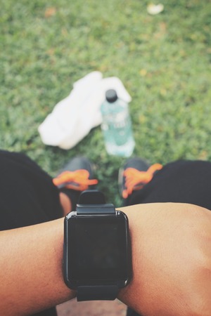 Selfie of smartwatch and sport shoes with water drink on green grassの写真素材