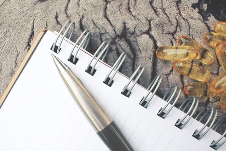 Blank notepad and pen with cod liver oil capsules on tableの写真素材