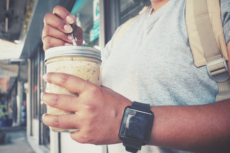 Woman tourist with ice coffee and backpack standing on roadの写真素材