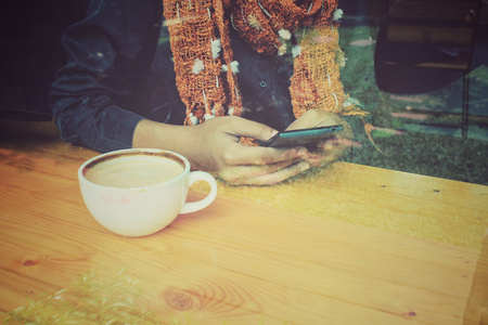 Woman drink coffee with smartphone sitting indoor in trendy urban cafe.の写真素材