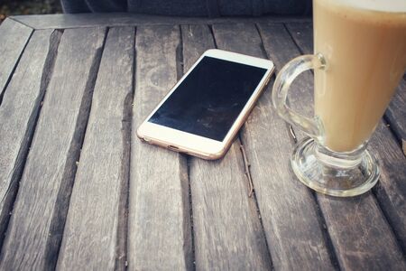 Vintage latte art coffee with smart phone on wood backgroundの写真素材