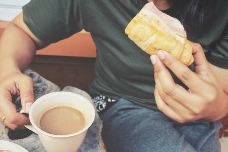 Woman drinking hot coffee with croissantsの写真素材