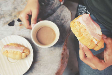 Woman drinking hot coffee with croissantsの写真素材