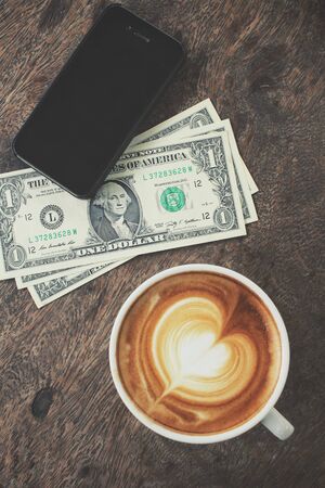 Vintage latte art coffee and smart phone with dollarsの写真素材