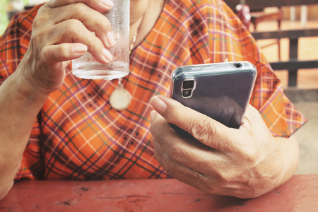 Senior drinking water with smart phoneの写真素材
