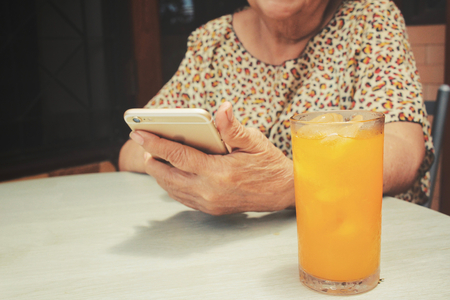 Senior woman using smart phone with orange drinkの写真素材