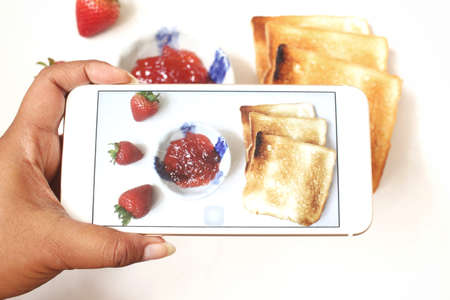 Taking a photo of toast bread and strawberry jam with smart phoneの写真素材