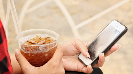 Woman drinking cola with using smart phoneの写真素材