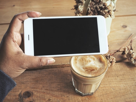 Smart phone on hand with coffee cupの写真素材