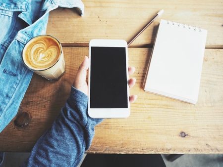 Woman using smart phone with blank notepad and coffee cup on office tableの写真素材