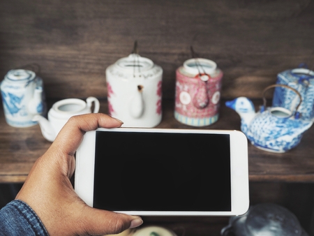 Smart phone on hand with tea potの写真素材