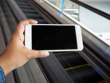 Smart phone on hand with escalator at shopping mall