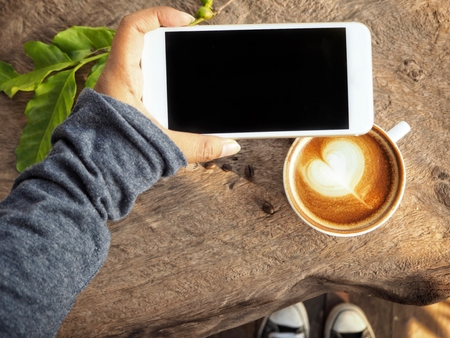 Smart phone on hand with latte art coffeeの写真素材