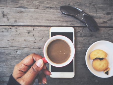 Woman drinking coffee cup with smart phone and cookie on table workの写真素材
