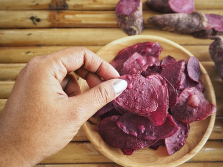 Eating purple sweet potato chips with handの写真素材