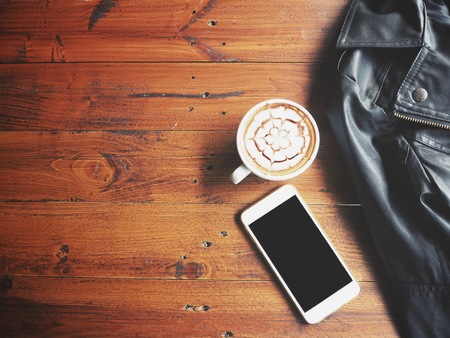 Coffee cup with smart phone and leather jacket on tableの写真素材