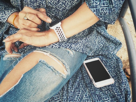 Woman playing smartwatch on hand with smart phoneの写真素材