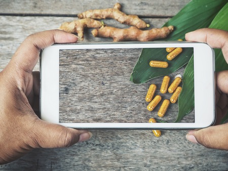 Taking a photo of turmeric capsule with smart phone on handの写真素材