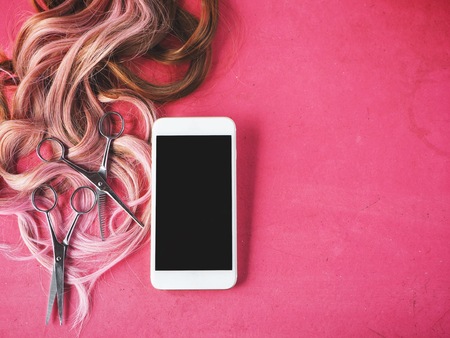Smart phone and hair cutting shears with wig on pink backgroundの写真素材