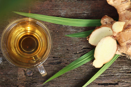 Hot tea on cup and ginger root on wood background