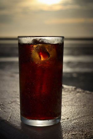 Cola drink with ice cubes and beach with blue sky