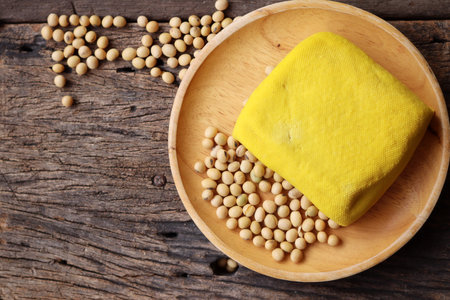 Soybeans and yellow tofu on wood background