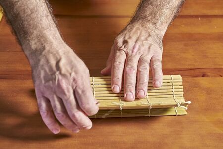 the cook spreads the rice on the seaweed sheet and rolls it with the bamboo mat from one endの写真素材