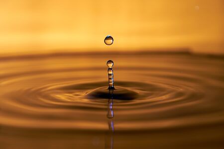 Water drop splashing macro with ripples on yellow color backgroundの写真素材