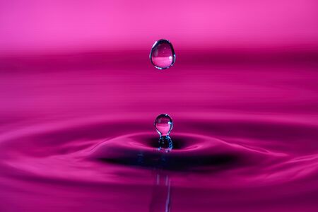 Water drop splashing macro with ripples on pink backgroundの写真素材