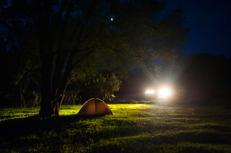 Romantic couple tourists have a rest at a campfire near illuminated tent under amazing night sky full of stars.の写真素材