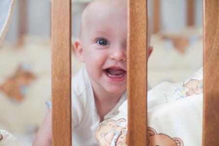 Cute smiling baby looking out of the crib. Funny kid in bedの写真素材