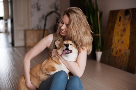 Smiling girl playing with her Welsh Corgi Pembroke puppy, happy cute dog. Dog lying on its owners...
