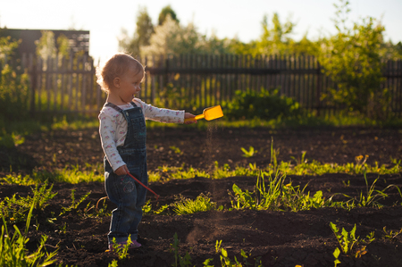 Baby sitting on the ground with shovel and rake in sunlight. Cute summer blond girl in the garden.の写真素材