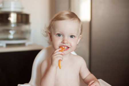 Baby girl eating Honeydew Melon. Funny  laughing child in the kitchen. Cheerful kid in the high chair.の写真素材