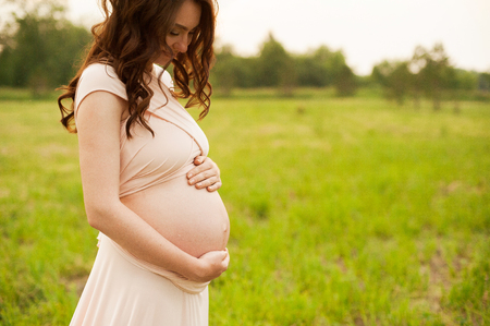 Portrait of a happy pregnant woman looking at her belly in a park at sunrise with a warm back light in the background.の写真素材