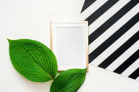 Gold photo frame with tropical leaves on black and white striped background. Mock up frame with copyspace. Flat lay, top viewの写真素材