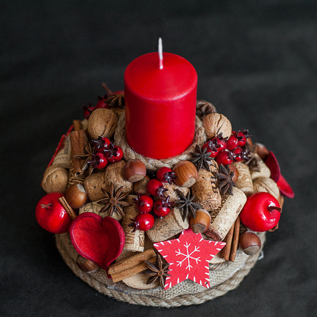 Red Christmas candle with berries, cinamon, nuts decorations on black backgoundの写真素材