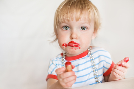 Little funny blond baby girl make up lips with mom's red lipstick. Learning to be woman. Happy childhood conceptの写真素材