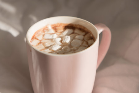 Close up pink cup of hot chocolate with marshmallows on the bed. Good morning, world.