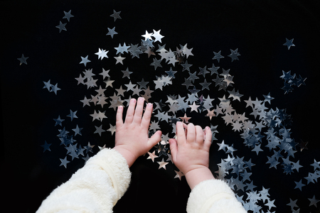 Christmas celebration. Cute baby play with decorations. Silver star sprinkles on black backgound.Top view.の写真素材