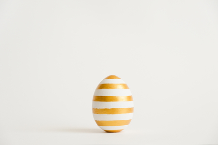 Easter golden with striped patternd egg  isolated on white background. Minimal easter concept. Happy Easter card with copy space for text.の写真素材