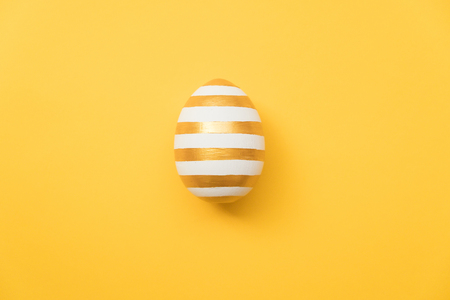 Easter golden with striped patternd egg on yellow background. Minimal easter concept. Happy Easter card with copy space for text. Top view, flatlay.の写真素材