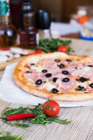 Flat lay with traditional Italian pizza with ham and olives on black stone table and various ingredients: mushrooms, tomatoes, oil, pepper, salt, basil, olive.の写真素材
