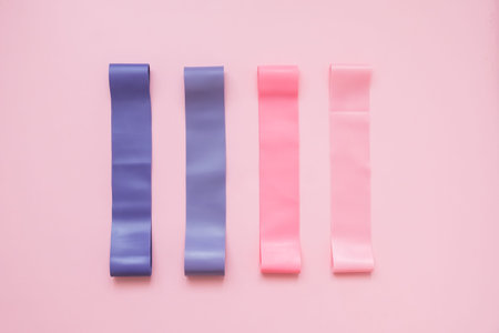 Colorful fitness gums on pink background. Elastic expanders of different colors