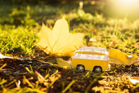 Autumn retro yellow van bus on autumn maple leaf background. Funny retro toy car. Autumn travel and vacation concept.の写真素材