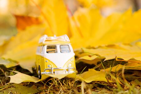 Autumn retro yellow van bus on autumn maple leaf background. Funny retro toy car with surfboard. Autumn travel and vacation concept.の写真素材