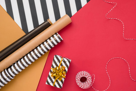 Christmas background with gift boxes, rope, papers rools and decorations on red. Preparation for...