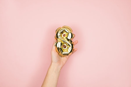 Gold foil balloons numeral 8 in femine hand on pink background. Happy Womens Day.